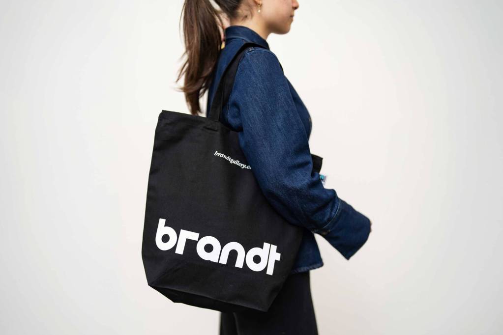 Omuzda taşınan siyah bez çanta üzerinde büyük beyaz brandt wordmark'ı